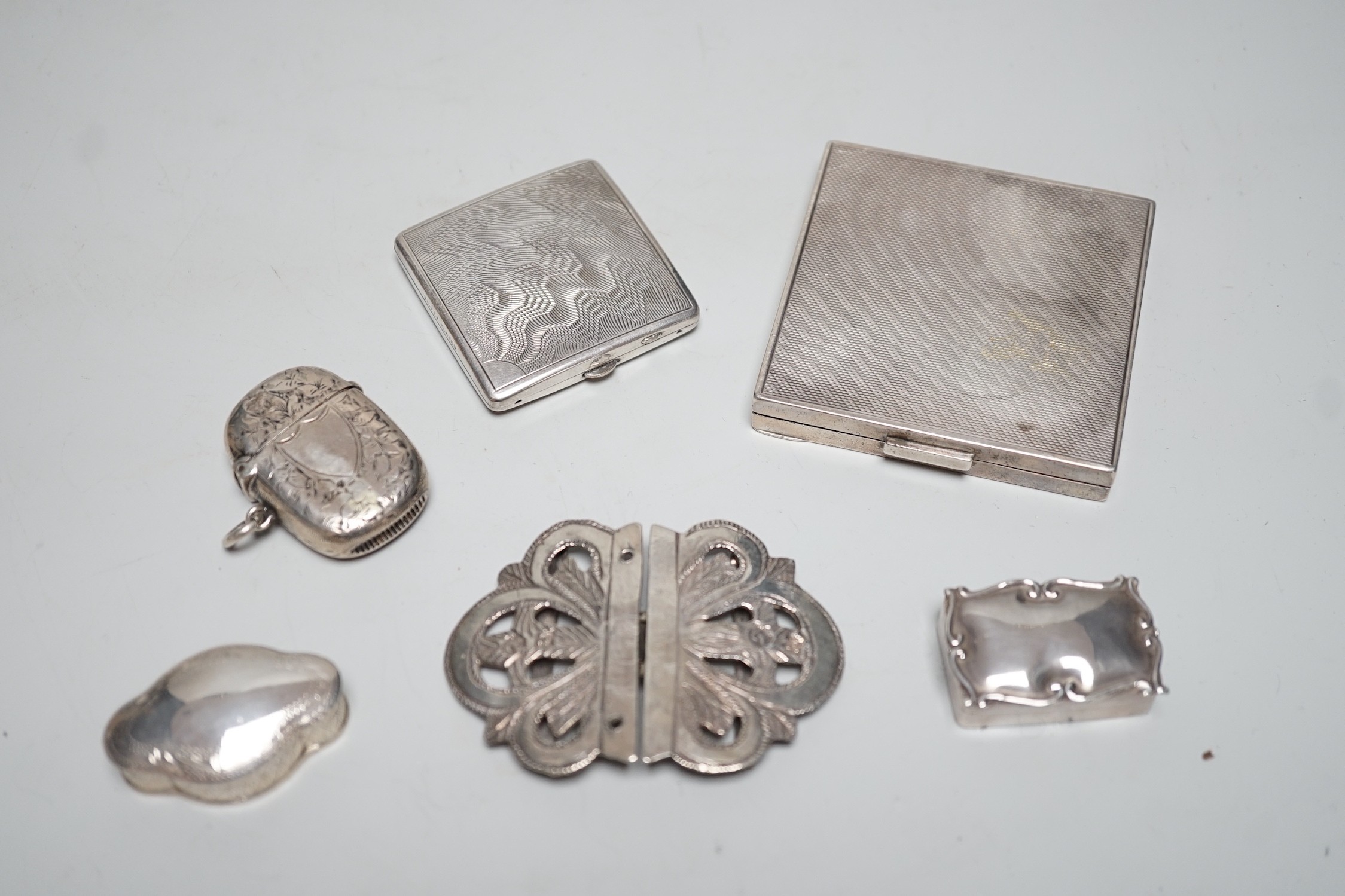 A George VI engine turned silver compact, 69mm, two modern silver pill boxes, a Persian white metal belt buckle, a silver vesta case and a base metal compact.